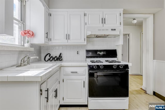 kitchen with tile countertops, under cabinet range hood, gas stove, and a sink