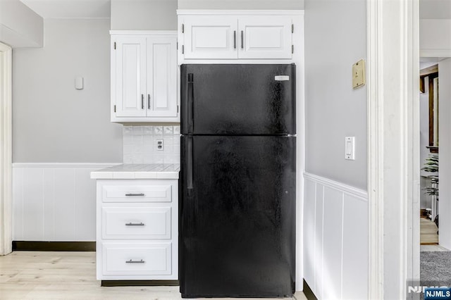 kitchen with white cabinets, tile counters, a wainscoted wall, and freestanding refrigerator