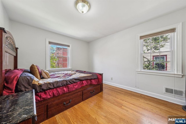 bedroom with light wood-type flooring, baseboards, visible vents, and multiple windows
