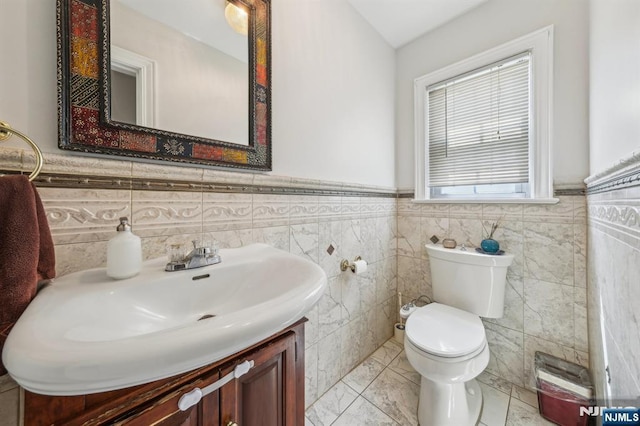 bathroom with tile walls, a wainscoted wall, vanity, and toilet