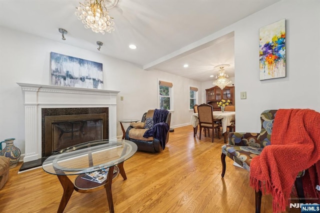 living room with recessed lighting, light wood-type flooring, baseboards, a glass covered fireplace, and a notable chandelier