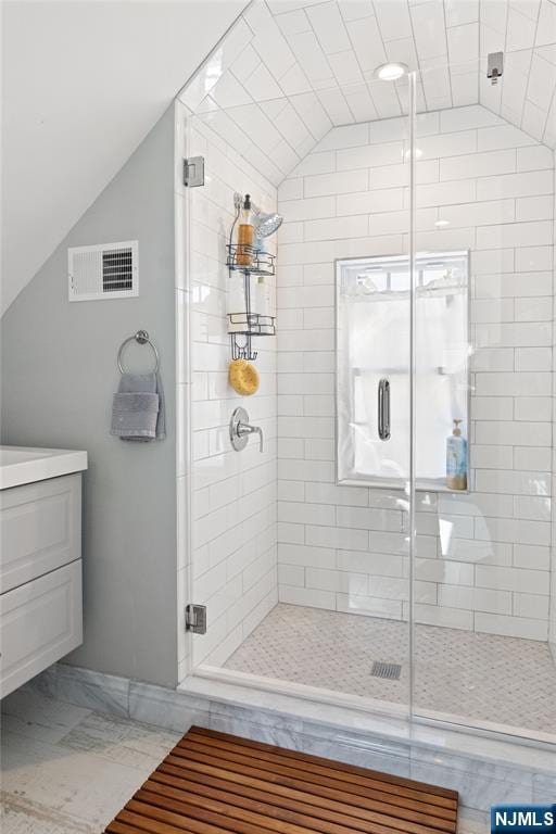 bathroom with vanity, a shower stall, vaulted ceiling, and visible vents
