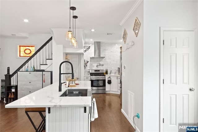 kitchen with backsplash, dark wood-style flooring, gas stove, a sink, and wall chimney exhaust hood