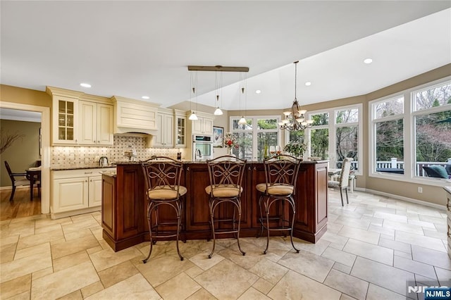 kitchen with cream cabinetry, backsplash, glass insert cabinets, stainless steel oven, and custom range hood