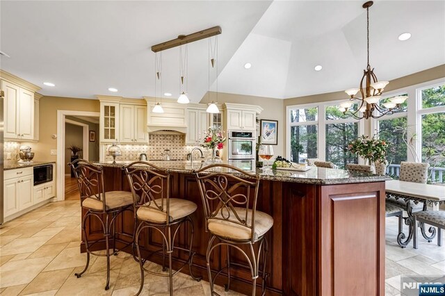 kitchen featuring a chandelier, black microwave, decorative backsplash, and cream cabinets