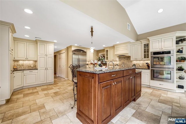 kitchen with stainless steel appliances, open shelves, dark stone counters, tasteful backsplash, and cream cabinets