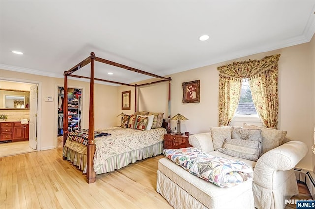 bedroom featuring light wood finished floors, ornamental molding, connected bathroom, a walk in closet, and baseboard heating