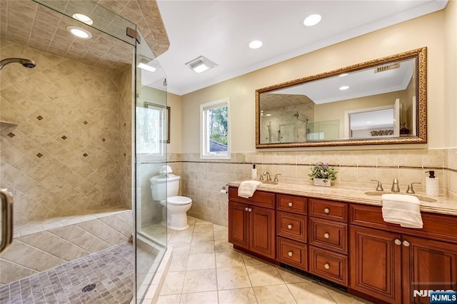 full bath featuring a tile shower, tile patterned flooring, double vanity, a sink, and tile walls