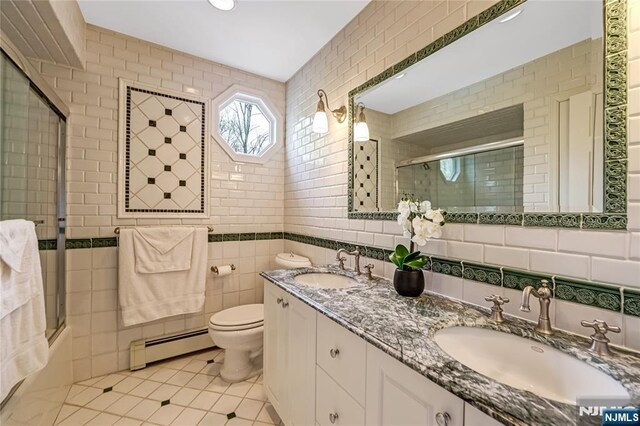 bathroom featuring a baseboard heating unit, tile walls, an enclosed shower, and a sink