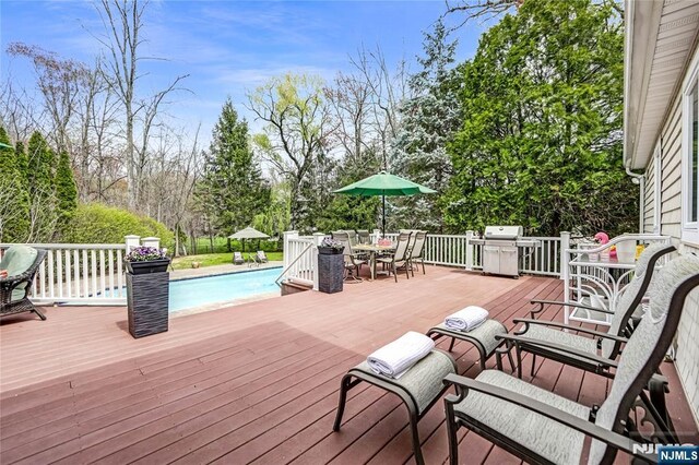 wooden deck featuring a grill, an outdoor pool, and outdoor dining space