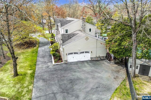 view of side of property featuring stairway, a shed, a chimney, driveway, and roof with shingles
