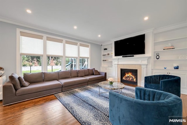 living area featuring recessed lighting, a glass covered fireplace, crown molding, and wood finished floors