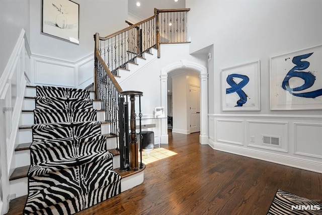 entrance foyer with stairway, a decorative wall, arched walkways, and dark wood-type flooring