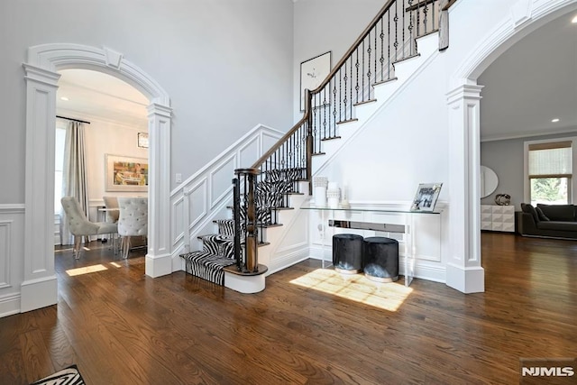 staircase with wood finished floors, decorative columns, crown molding, a decorative wall, and arched walkways