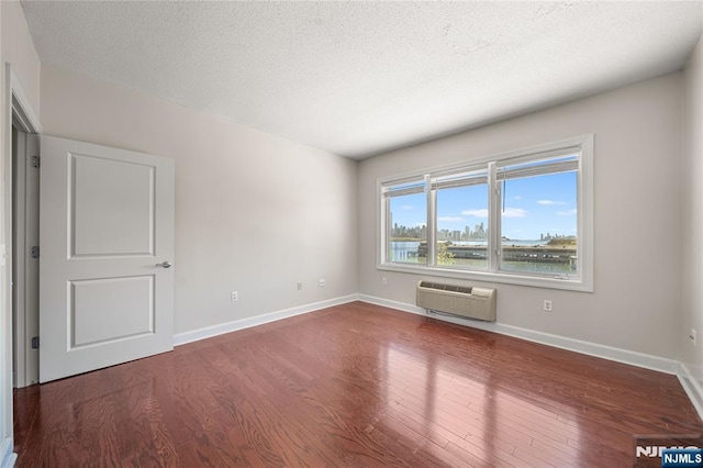 spare room with a textured ceiling, baseboards, a wall mounted AC, and wood finished floors