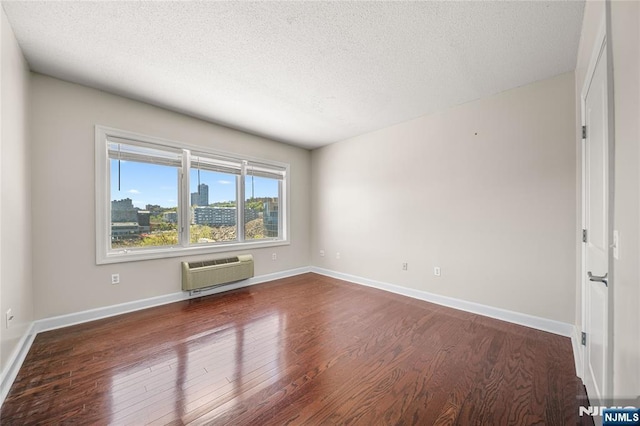 unfurnished room with baseboards, a wall mounted air conditioner, a textured ceiling, and wood finished floors