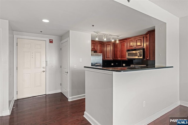 kitchen featuring dark wood-style flooring, dark countertops, refrigerator, baseboards, and stainless steel microwave