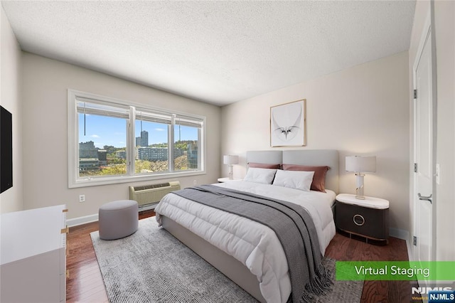 bedroom featuring baseboards, a wall unit AC, a textured ceiling, and wood finished floors