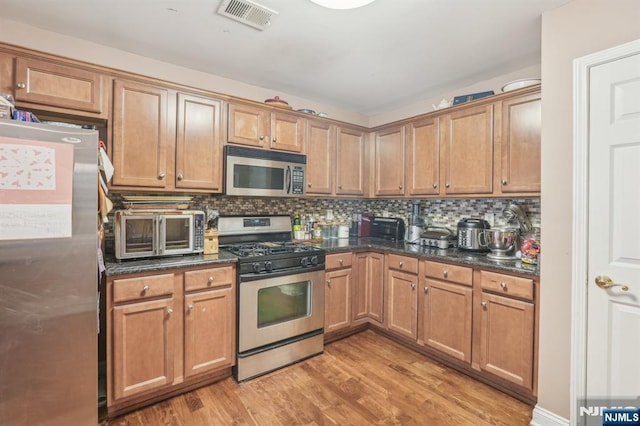 150 Blue Heron Dr, Secaucus, NJ 07094 - kitchen featuring appliances with stainless steel finishes, light wood-style flooring, decorative backsplash, brown cabinetry, and dark stone counters