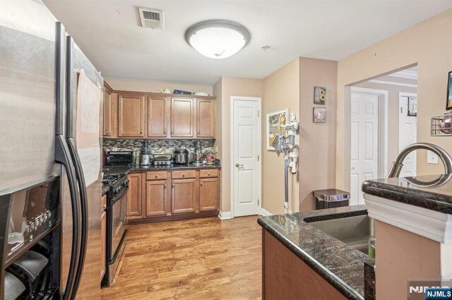 150 Blue Heron Dr, Secaucus, NJ 07094 - kitchen featuring appliances with stainless steel finishes, light wood-style floors, dark stone countertops, decorative backsplash, and brown cabinetry