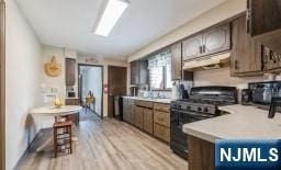kitchen with dark brown cabinetry, black gas stove, light countertops, a peninsula, and light wood-style flooring