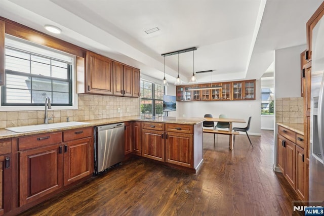 kitchen with dark wood finished floors, dishwasher, a sink, a raised ceiling, and a peninsula