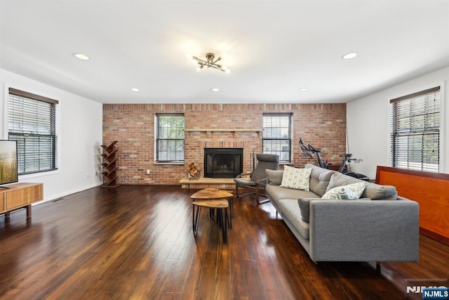 living room with a brick fireplace, brick wall, a healthy amount of sunlight, and dark wood-type flooring