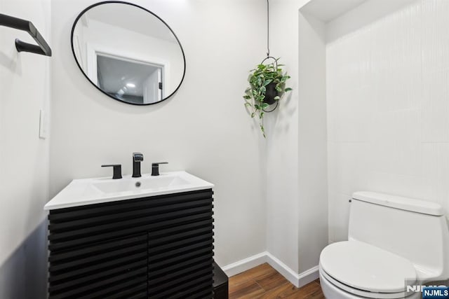 half bathroom with baseboards, wood finished floors, toilet, and vanity