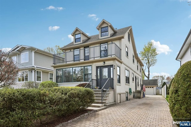 view of front facade featuring decorative driveway, an outdoor structure, a balcony, entry steps, and stucco siding