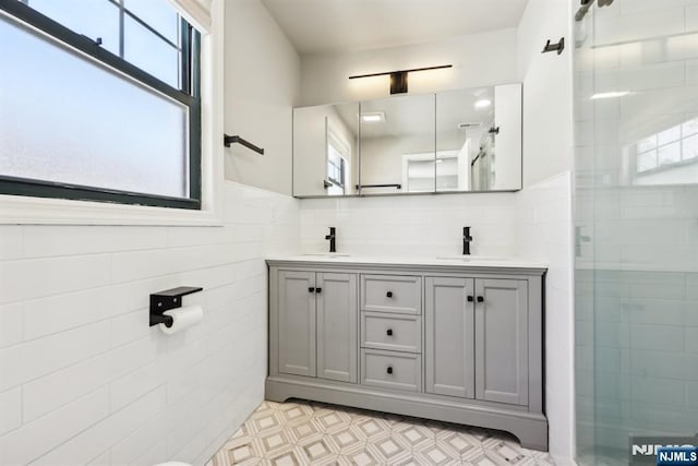 bathroom with tiled shower, double vanity, tile walls, and a sink