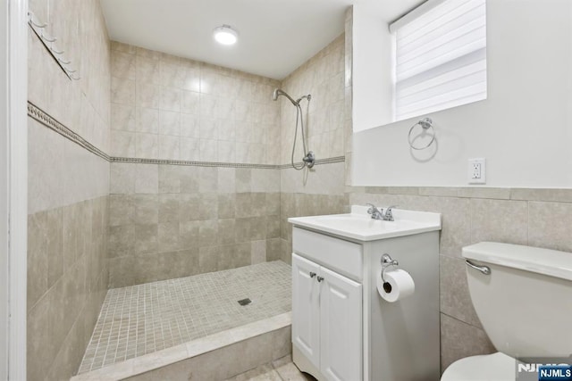 bathroom with toilet, tile walls, a tile shower, and vanity