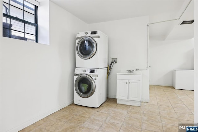 washroom featuring visible vents, cabinet space, a sink, baseboards, and stacked washer and clothes dryer