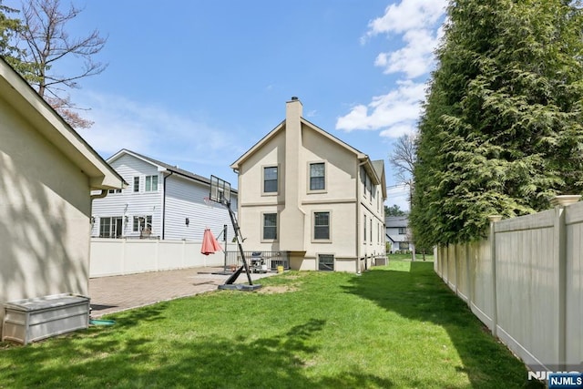back of house with fence, stucco siding, a chimney, a lawn, and a patio