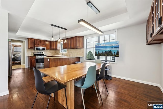 dining space featuring a tray ceiling, dark wood finished floors, and baseboards