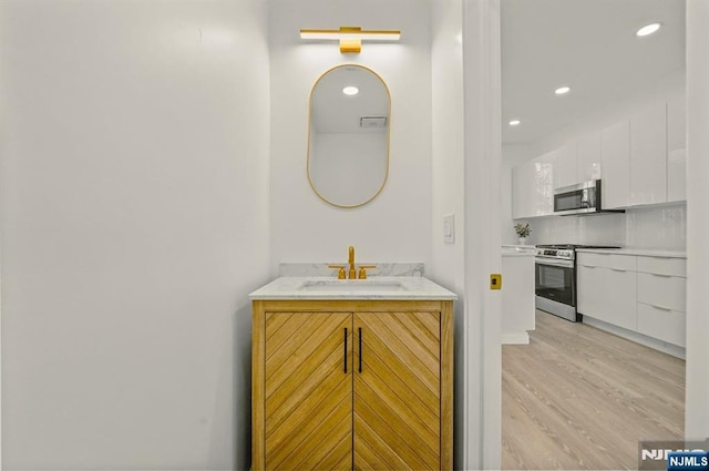 bathroom with wood finished floors, vanity, and recessed lighting