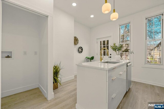 kitchen with a sink, light countertops, dishwasher, light wood finished floors, and hanging light fixtures