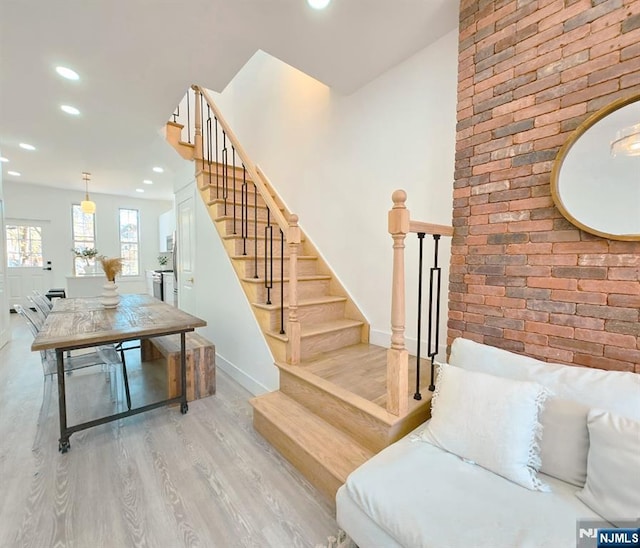 stairs featuring baseboards, wood finished floors, recessed lighting, and brick wall
