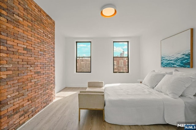 bedroom with wood finished floors and brick wall