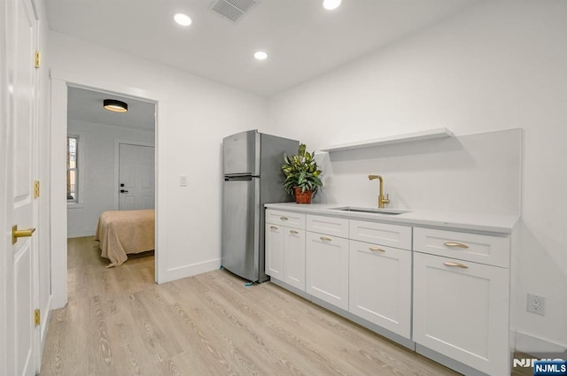 kitchen with a sink, visible vents, light wood-style flooring, white cabinets, and freestanding refrigerator