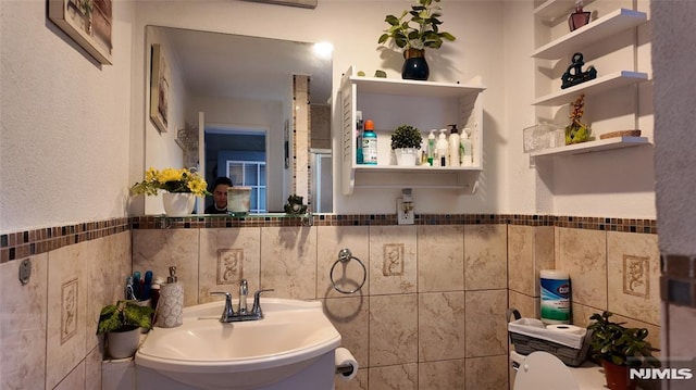bathroom featuring wainscoting, a sink, and tile walls