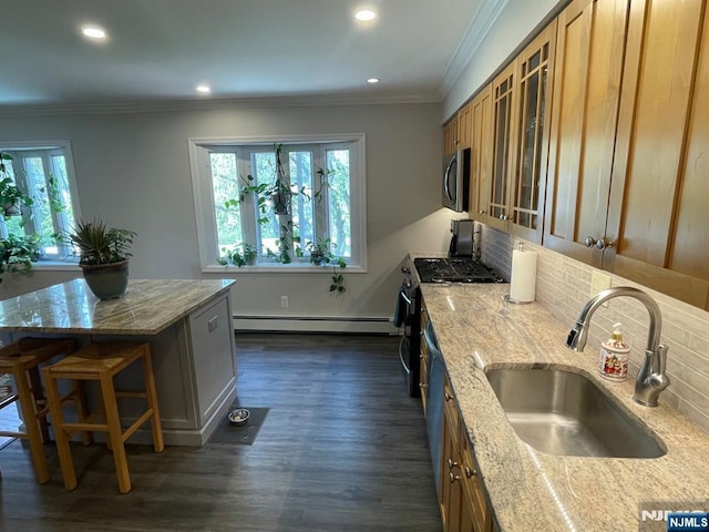 kitchen with appliances with stainless steel finishes, brown cabinets, a sink, a baseboard heating unit, and glass insert cabinets