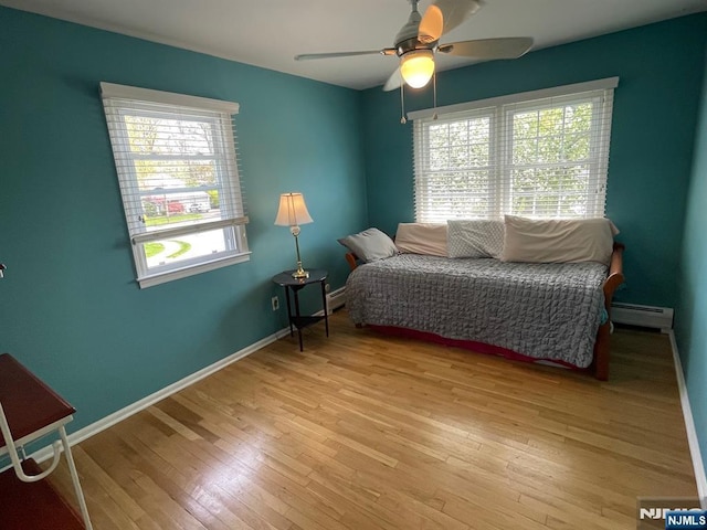 bedroom with light wood-type flooring, a ceiling fan, baseboards, and baseboard heating