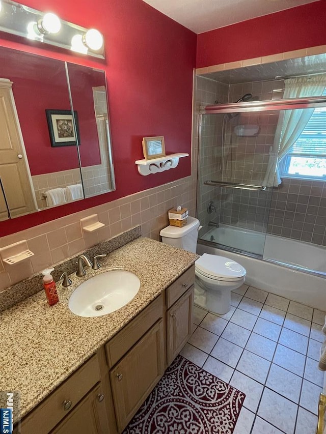 full bath with tile patterned flooring, vanity, toilet, tile walls, and bath / shower combo with glass door