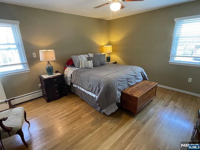bedroom featuring light wood-style floors, multiple windows, and a baseboard radiator