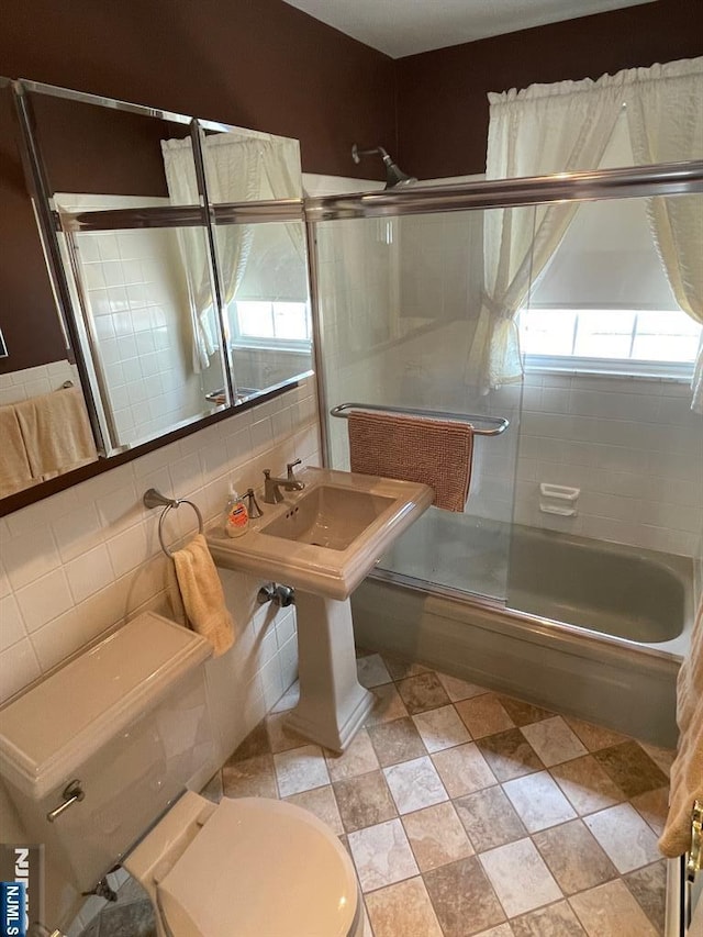 bathroom featuring toilet, tile walls, and bath / shower combo with glass door