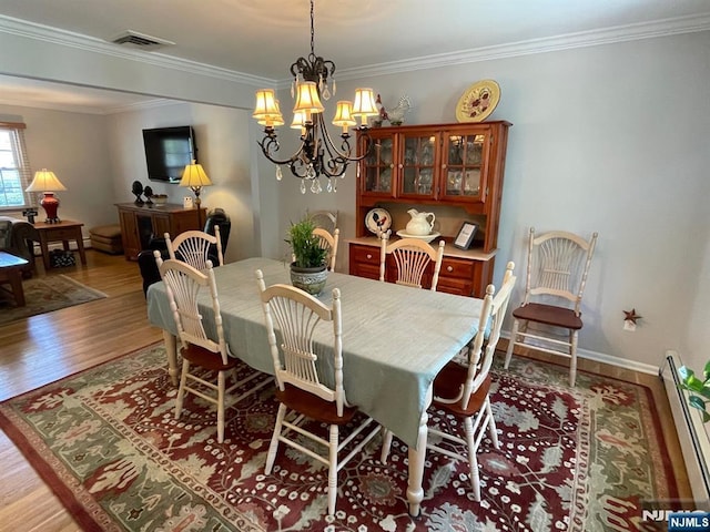 dining space featuring visible vents, crown molding, a baseboard heating unit, a chandelier, and light wood-style flooring