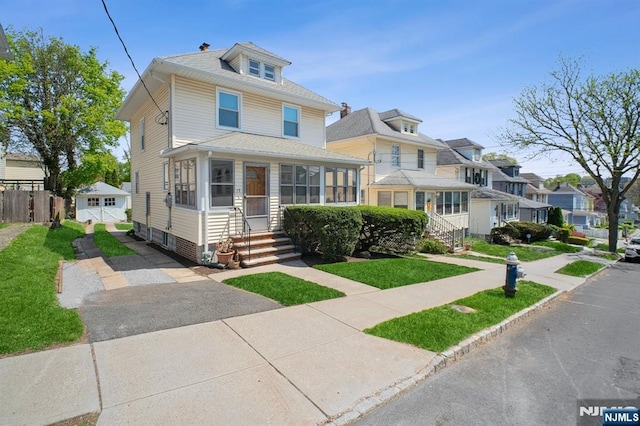 american foursquare style home featuring entry steps, an outdoor structure, a front yard, and a sunroom
