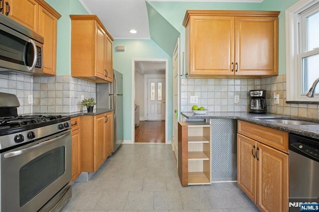 kitchen with dark stone counters, a sink, stainless steel appliances, and baseboards