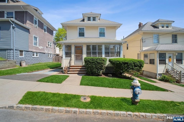 american foursquare style home with entry steps, a front lawn, and a sunroom