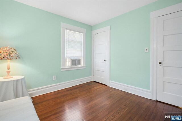 unfurnished bedroom featuring cooling unit, baseboards, and dark wood finished floors